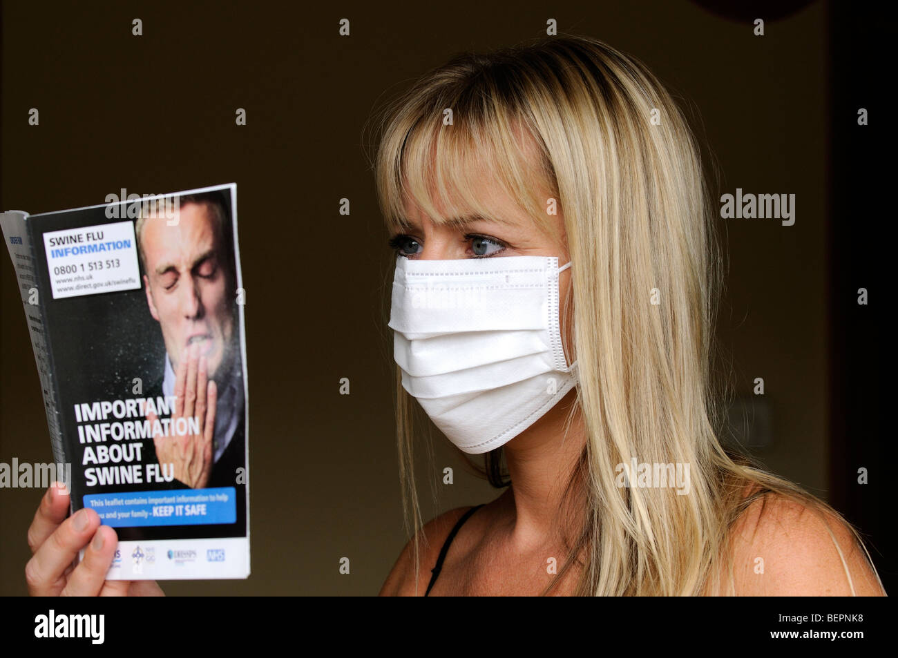 Portrait of a woman wearing a medical mask and reading Swine Flu information booklet Stock Photo