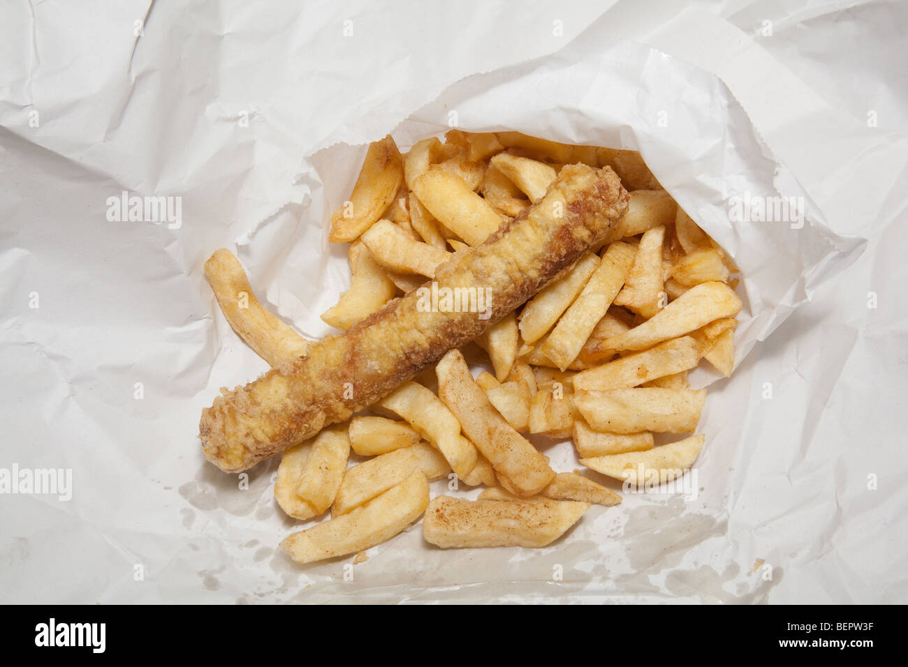 Take away sausage or saveloy and chips wrapped in white paper. Stock Photo
