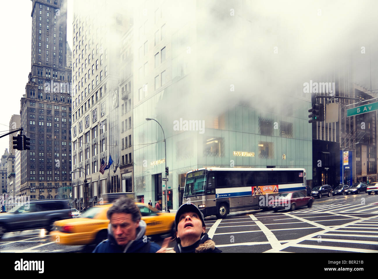 Winter view looking up 5th Avenue New York City from the corner of W 57th Street with shoppers and yellow cabs and steam. Stock Photo