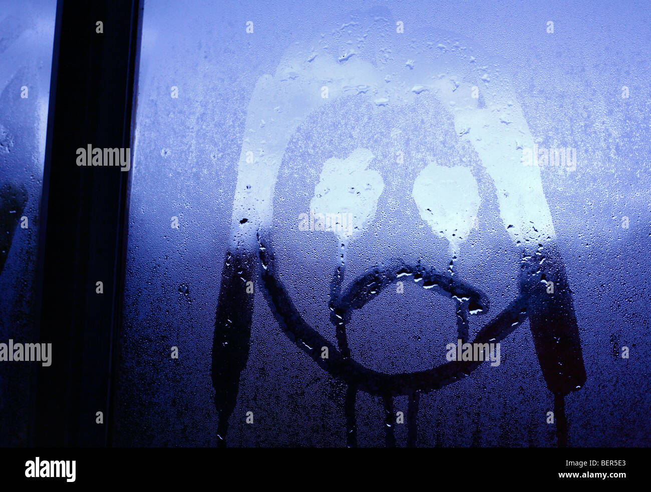 An unhappy childlike face drawn onto window condensation. Stock Photo