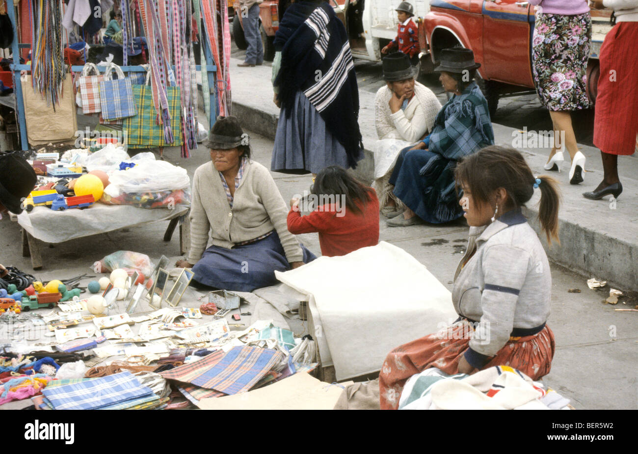 Three women one older to younger sit on ground behind stall of trinkets, bags and other general items. Stock Photo