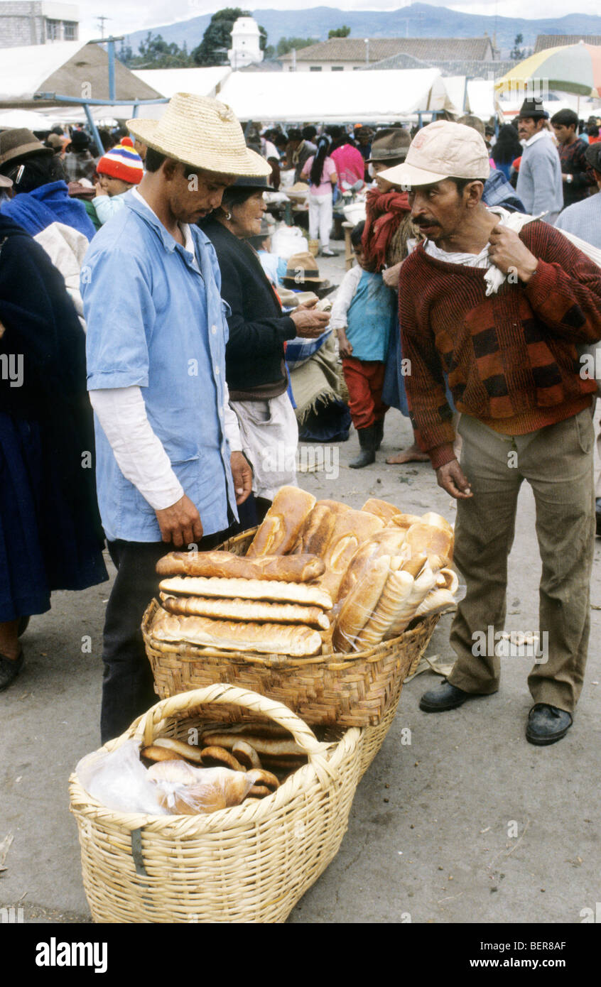 Man in straw hat stands before large basket full of long slightly flattened loaves of bread.  Ecuadorian Highland Market. Stock Photo