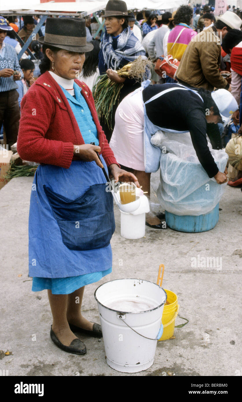 Woman selling drinks from a large enamel bucket at her feet.  Ecuador highlands local market. Stock Photo