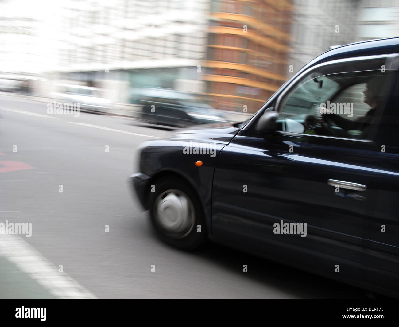 A traditional black cab or London taxi is driven in central London Stock Photo