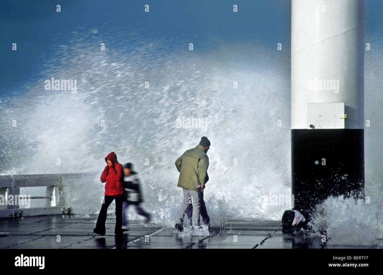 Curious tourists running away from huge wave during winter storm at the North Sea, Ostend, Belgium Stock Photo