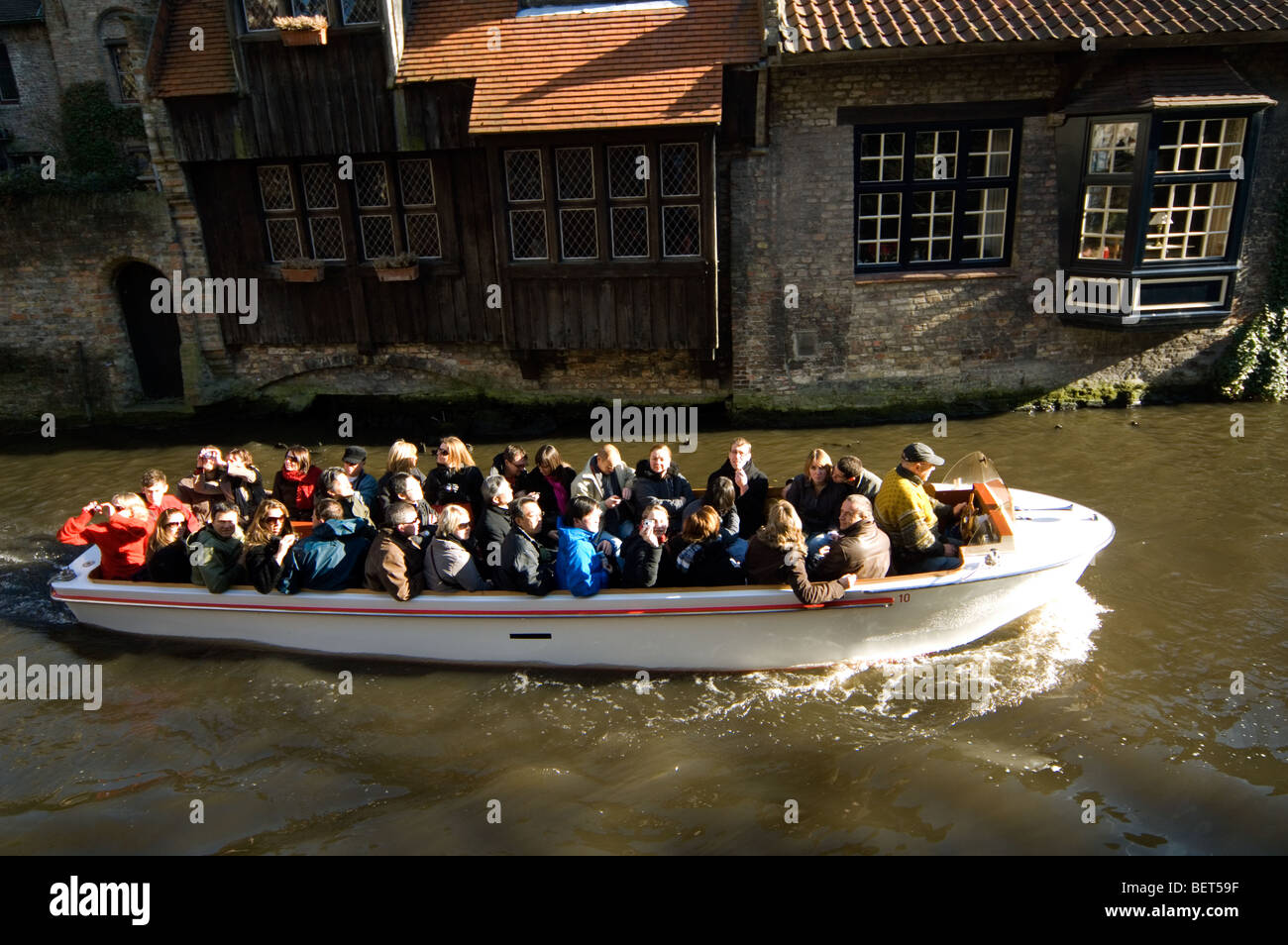 Tourists in boat and wooden rear elevation along canal in Bruges, Belgium Stock Photo