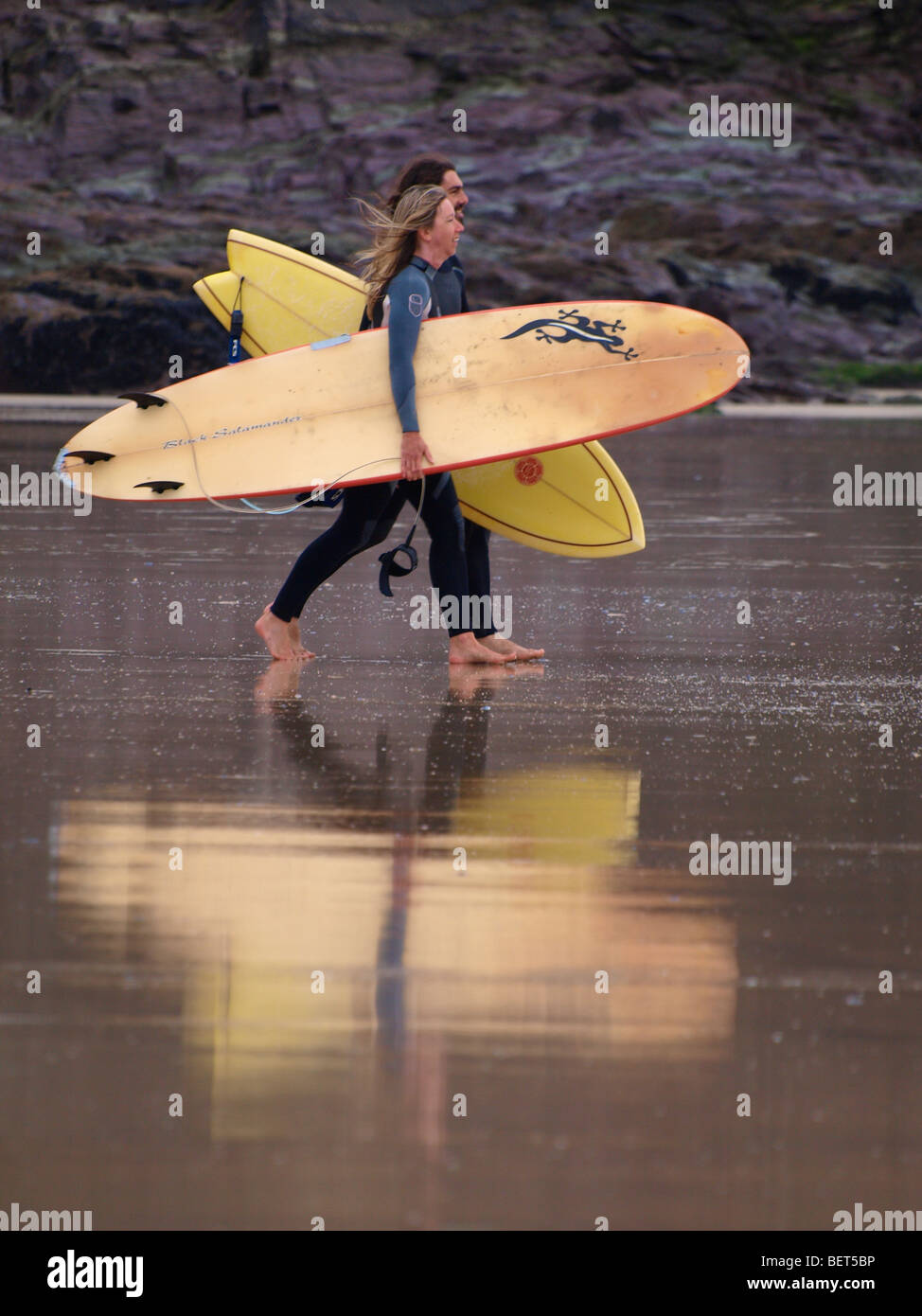 Two surfers heading for the sea with reflection in the wet sand. Stock Photo