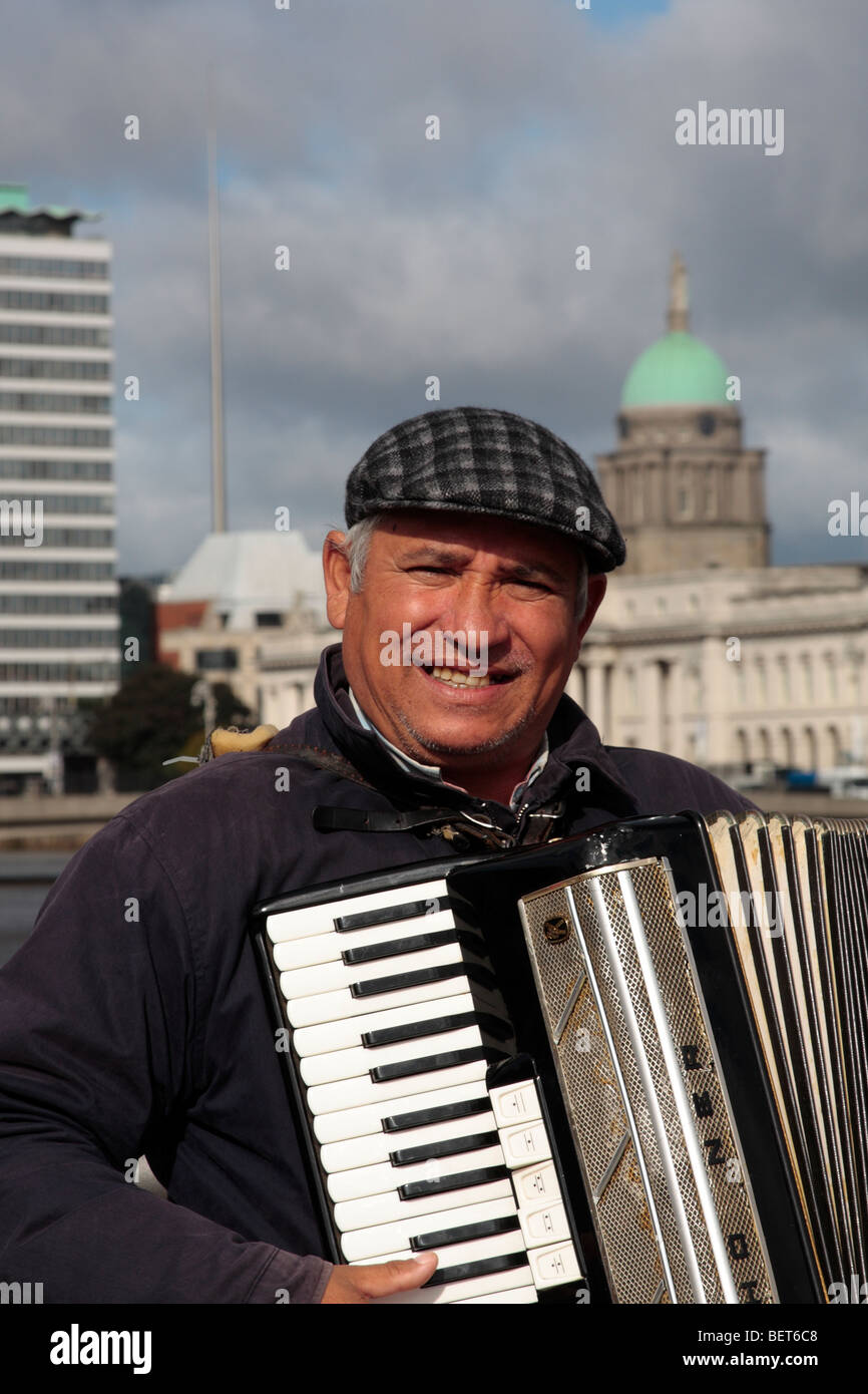 An accordion player busking on the Sean O Casey bridge with the Liberty Hall, the Millennium Spire and the Customs House behind Stock Photo