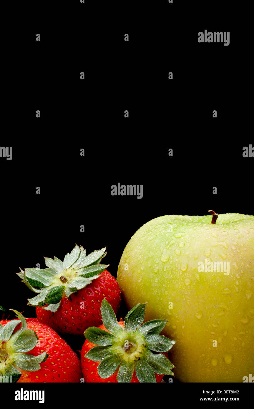 A green apple and red strawberries on black Stock Photo