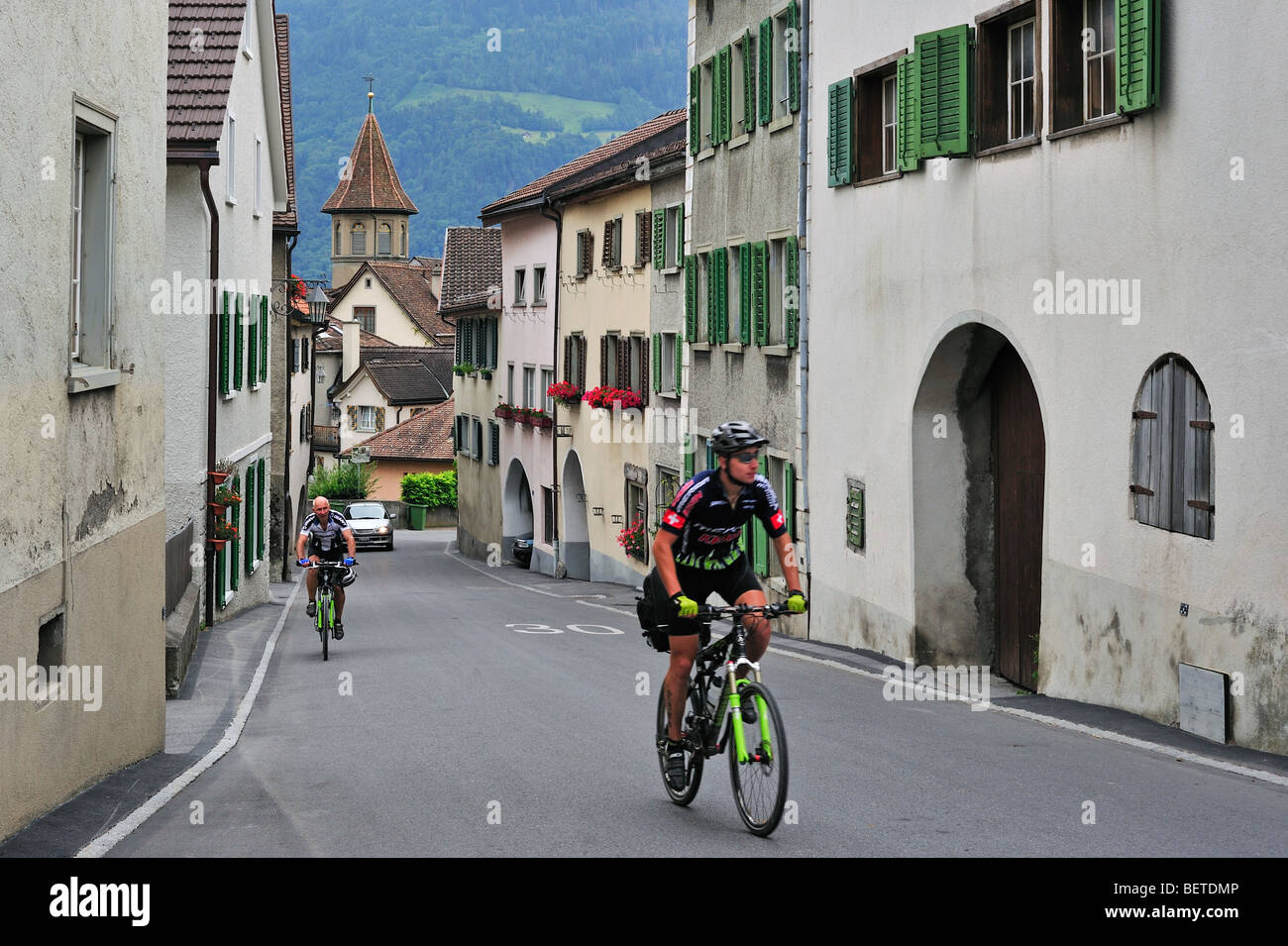 Cyclists riding through the Alpine village Maienfeld in Graubünden / Grisons, Swiss Alps, Switzerland Stock Photo