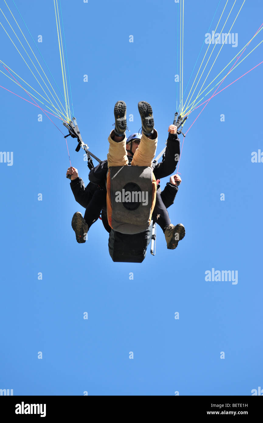 Tandem paraglider, worm's eye view on pilot and passenger against blue sky Stock Photo