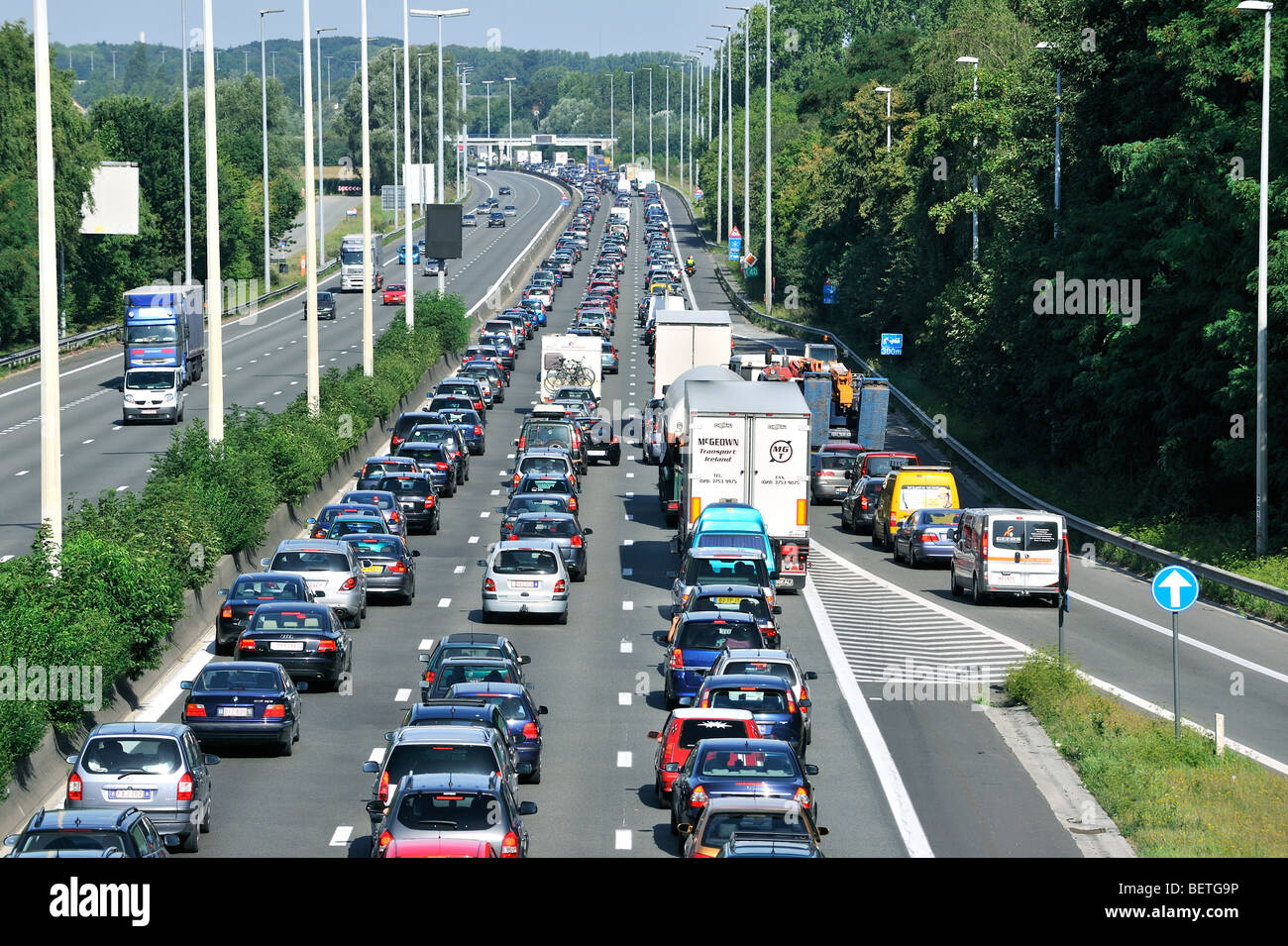 Cars and trucks queueing in highway lanes at approach slip road during traffic jam on motorway during summer holidays, Belgium Stock Photo