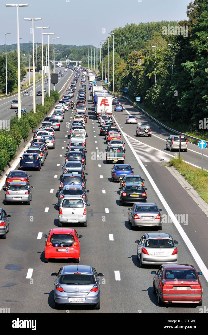 Cars and trucks queueing in highway lanes at approach slip road during traffic jam on motorway during summer holidays, Belgium Stock Photo