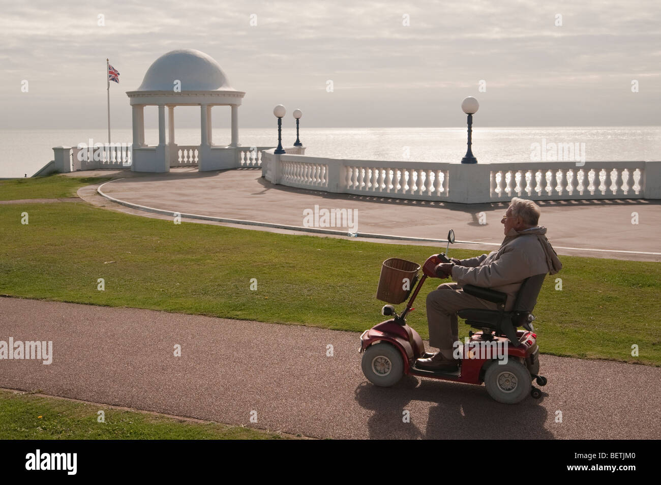 Old man drives an electric mobility scooter near the seafront Bexhill on Sea East Sussex England UK Stock Photo