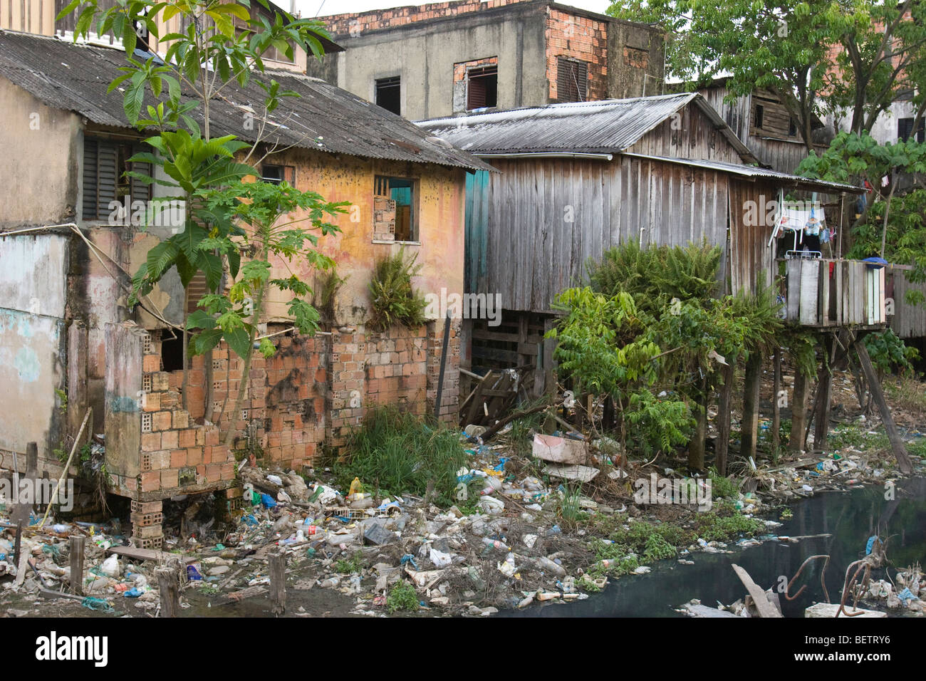 a small polluted creek flows by a rrun down shanty town in a third world barrio in the Amazon city of Manaus in Brazil Stock Photo
