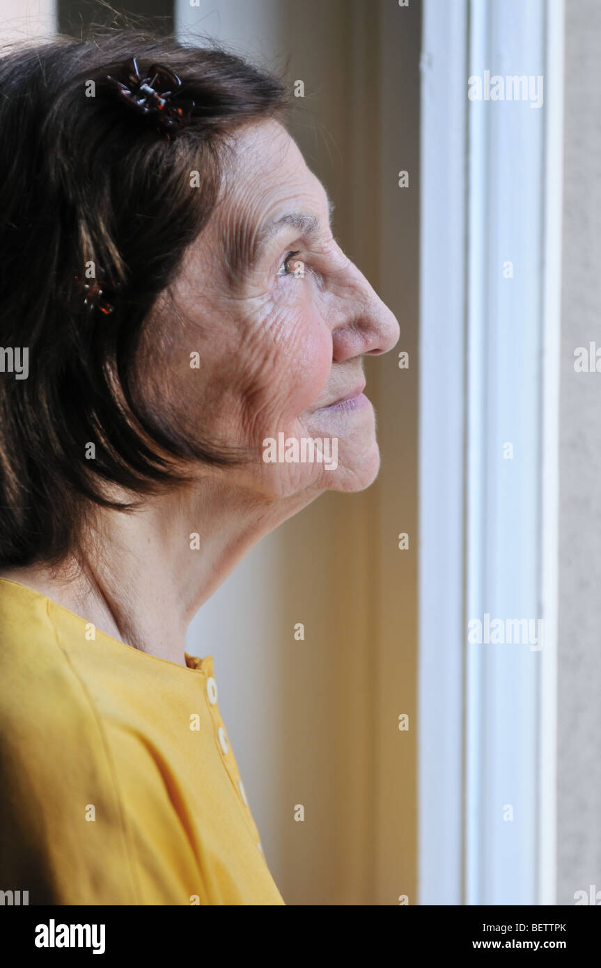 Solitude concept - sad 80s senior woman looking through window at home Stock Photo