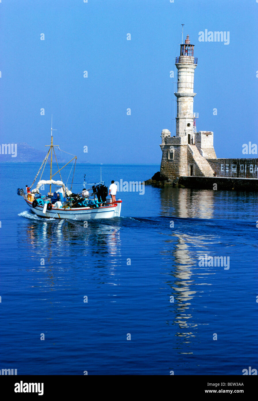 Fishing boat leaving in the morning from port town of Chania (Xhania) with lighthouse on north coast of Crete Stock Photo