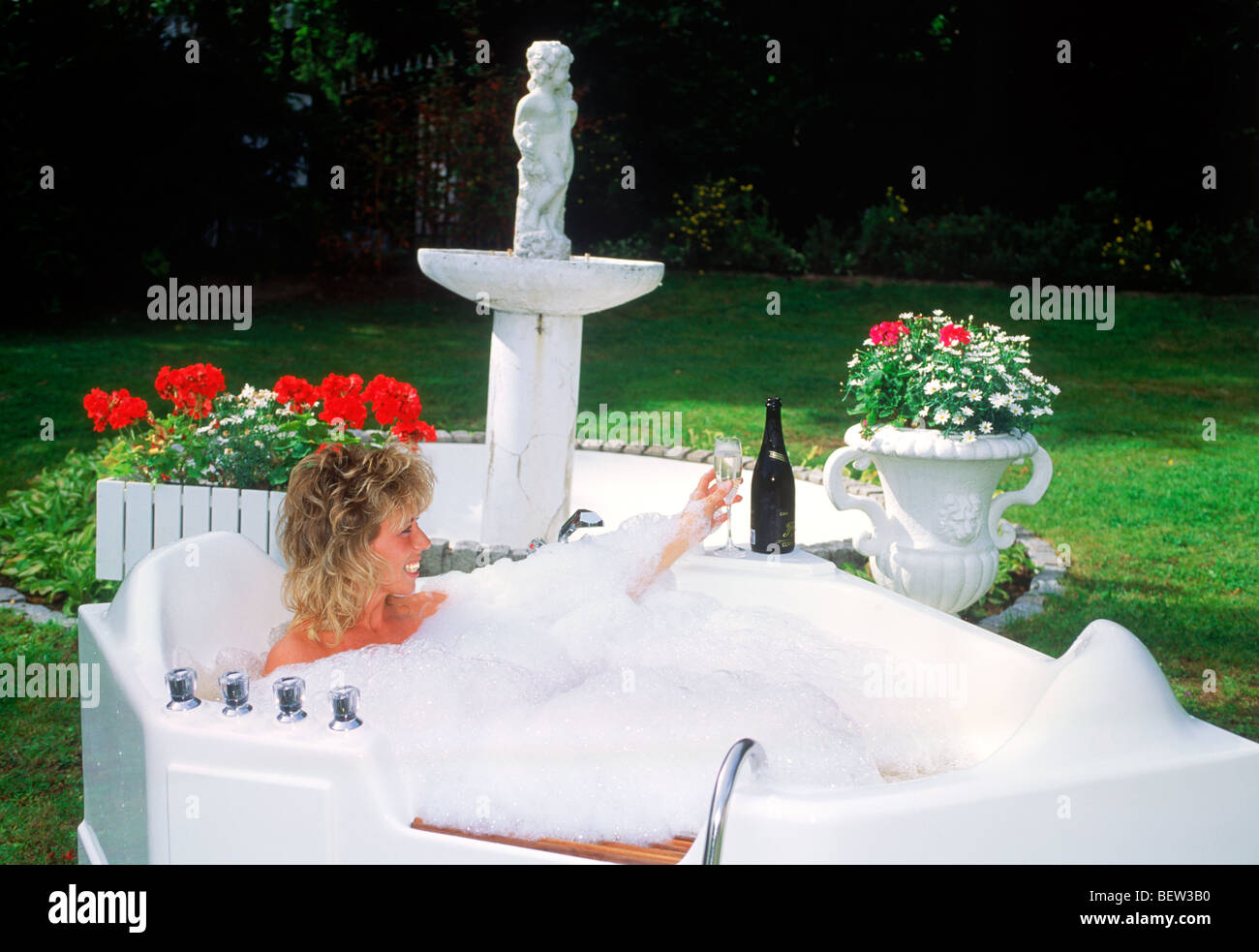 Women soaking in outdoor bathtub with bubbles and glass of champagne Stock Photo