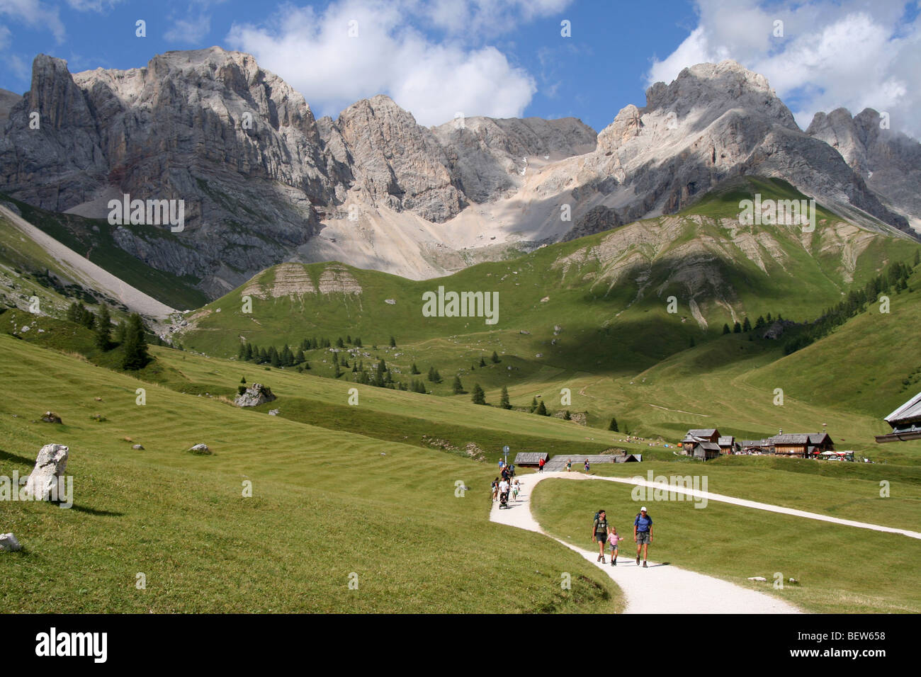 family strolling on lane near timber chalets for haymaking in the Italian Dolomites summer Stock Photo