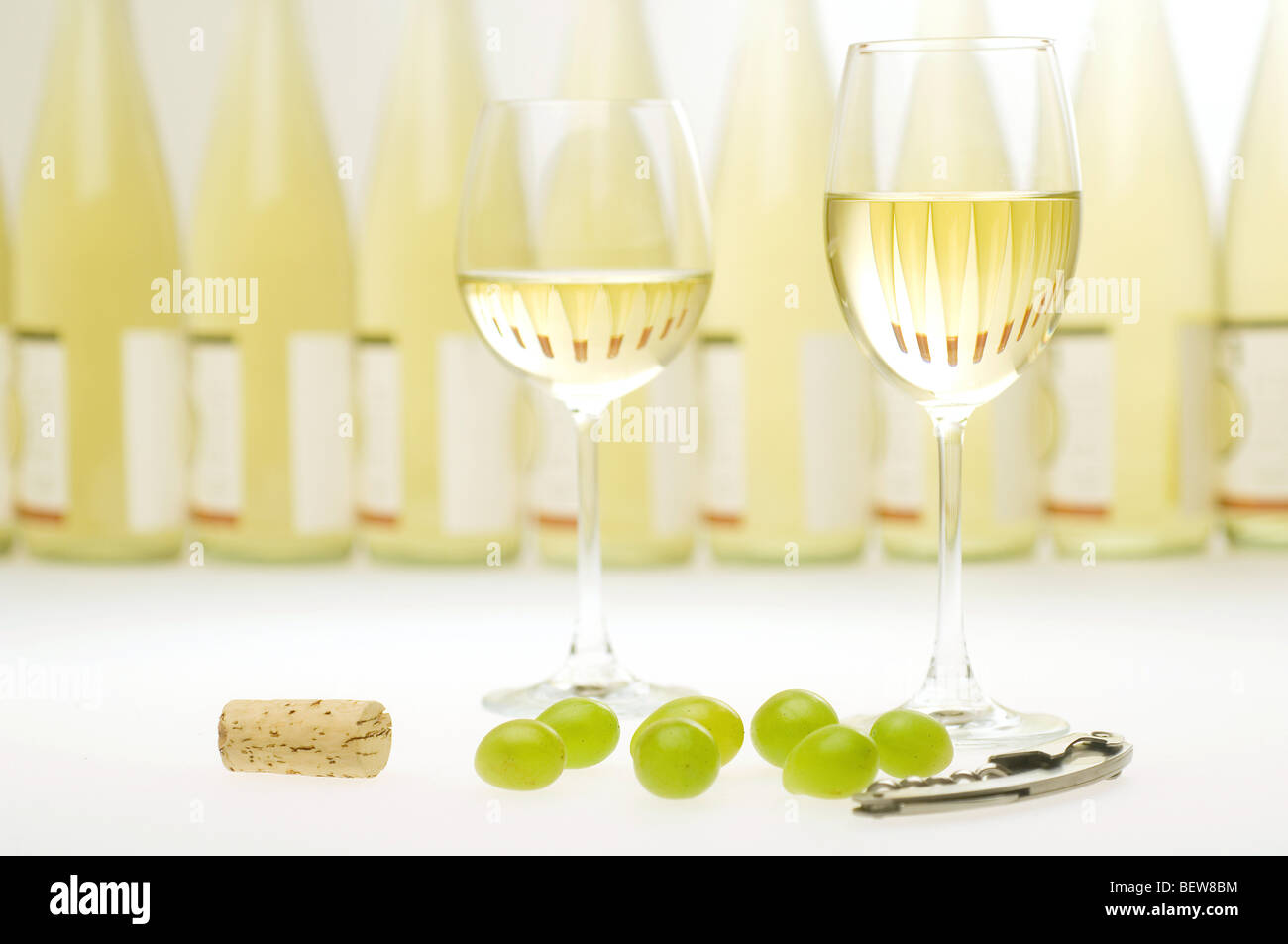 Two filled white wine glasses in front of a row of wine bottles, still life Stock Photo