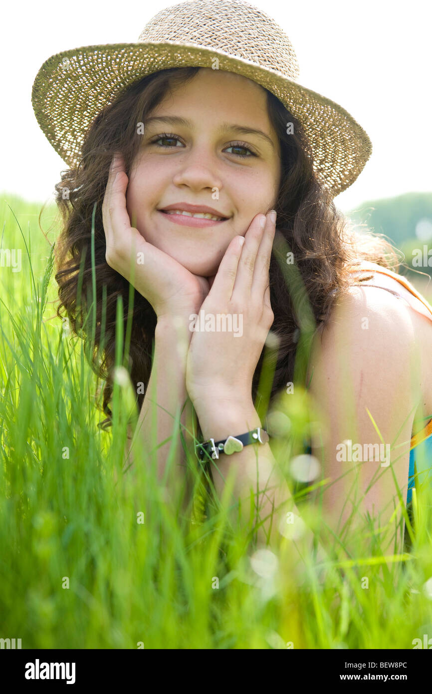 Young girl with straw hat lying in a rich green meadow, eye contact
