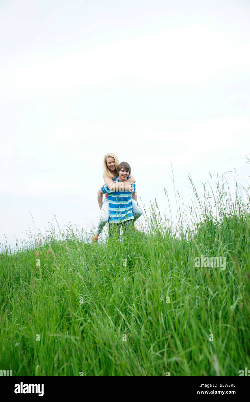 Man carrying woman piggyback through a meadow, low angle view Stock Photo