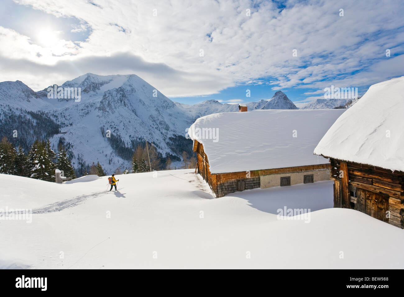 Woman with skis on a snowy mountain pasture with timber houses, Zederhaus, Salzburg, Austria Stock Photo