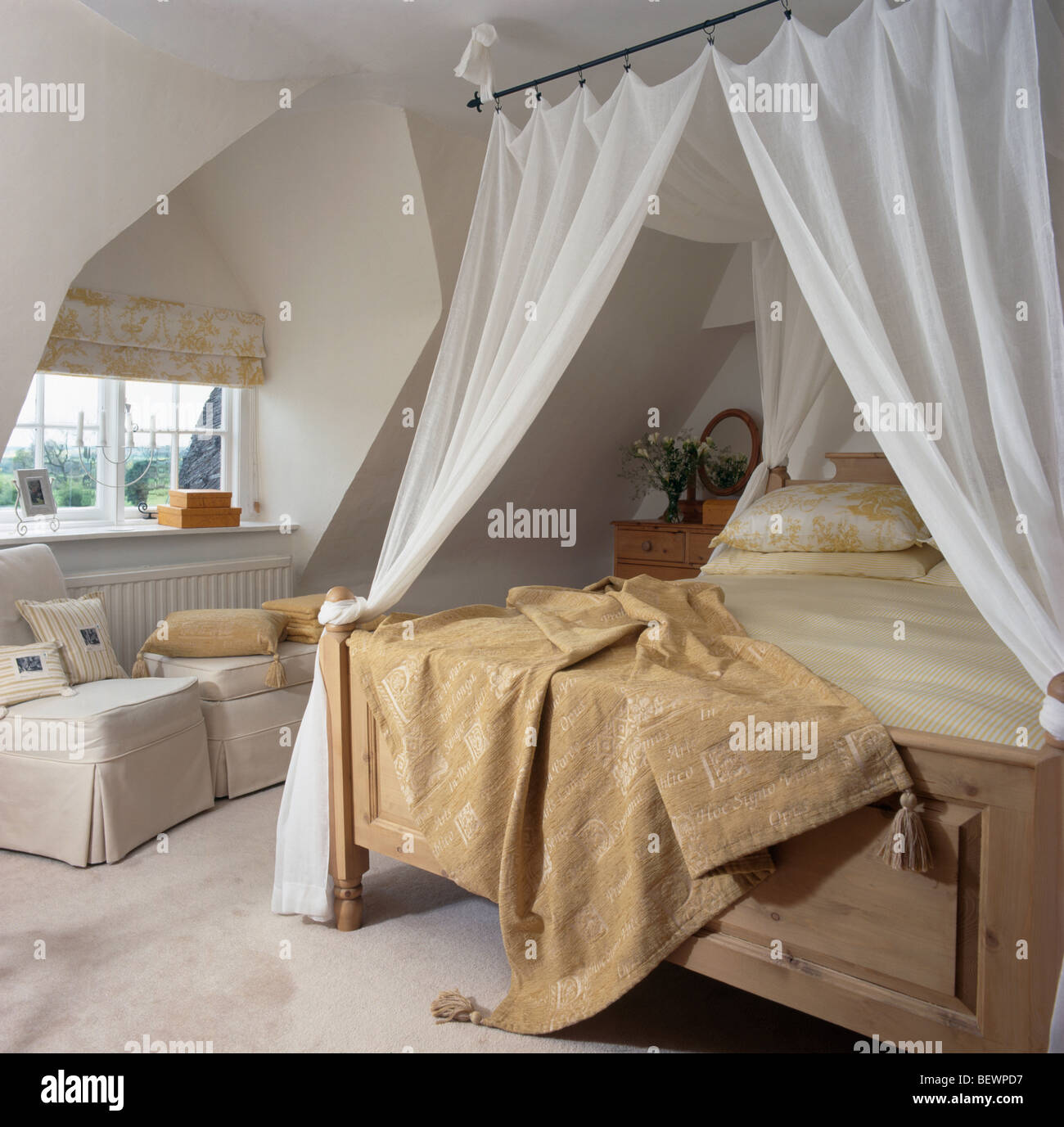 Beige chenille throw on wooden bed with white drapes in cream attic bedroom with dormer window Stock Photo
