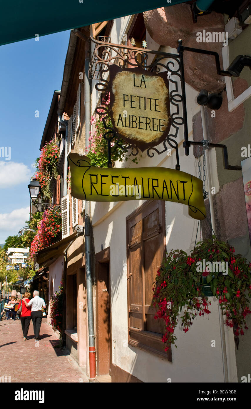Sign for 'La Petite Auberge' restaurant with couple strolling in background Kaysersberg Alsace France Stock Photo