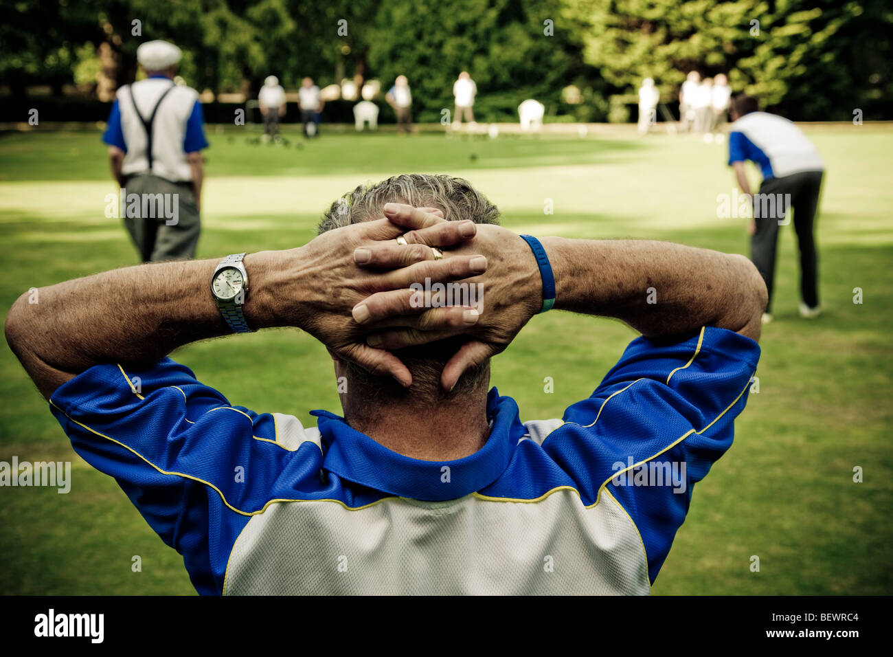 A Lawn Bowls player  with hands crossed behind head watches a bowling tournament at Southwark Park Club London SE1 Stock Photo