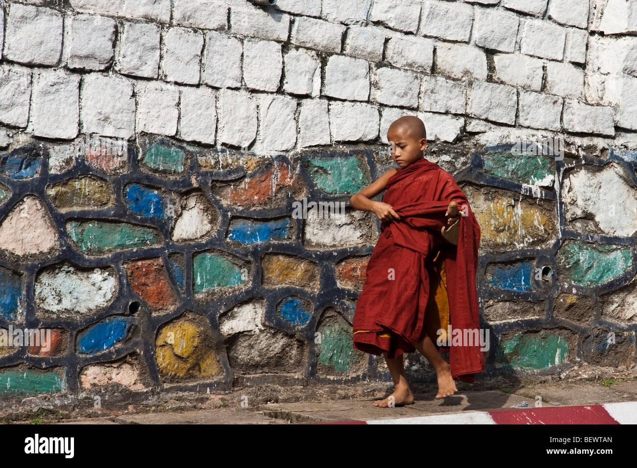 a young novice monk rings a chime during morning alms Stock Photo