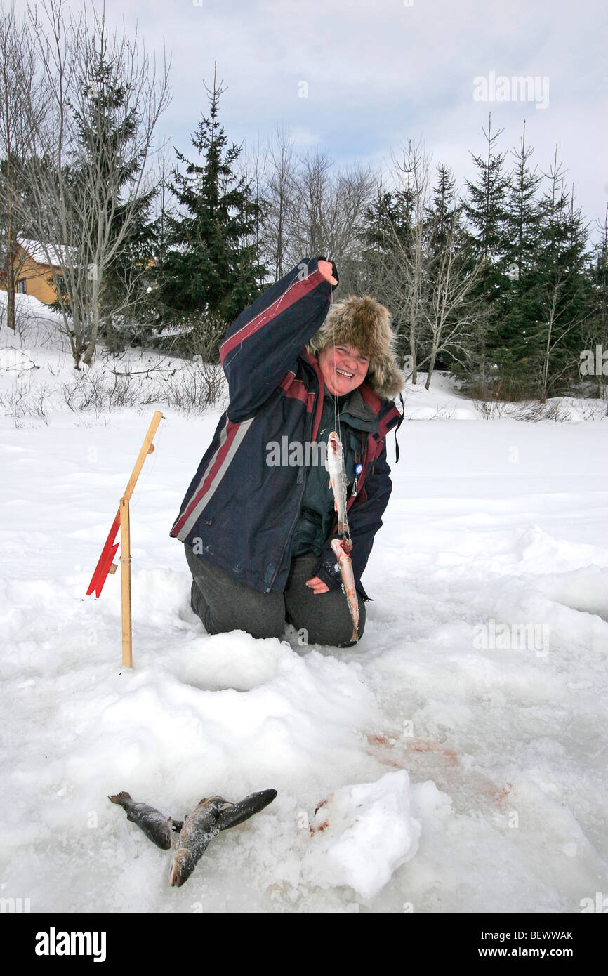 Woman pulls trout from lake while ice fishing in Duchenay Park in Quebec Stock Photo