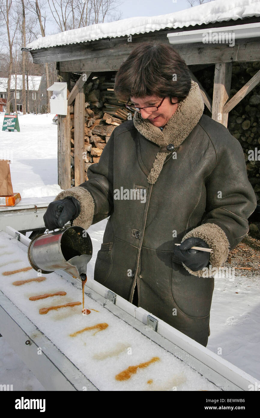 Woman pours liquid maple sugar on snow to make maple taffy at sugar