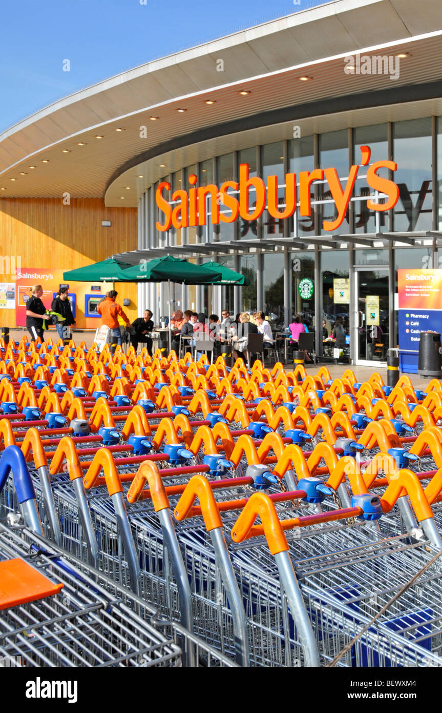 Sainsburys supermarket trolley park and entrance with Starbucks coffee shop Stock Photo