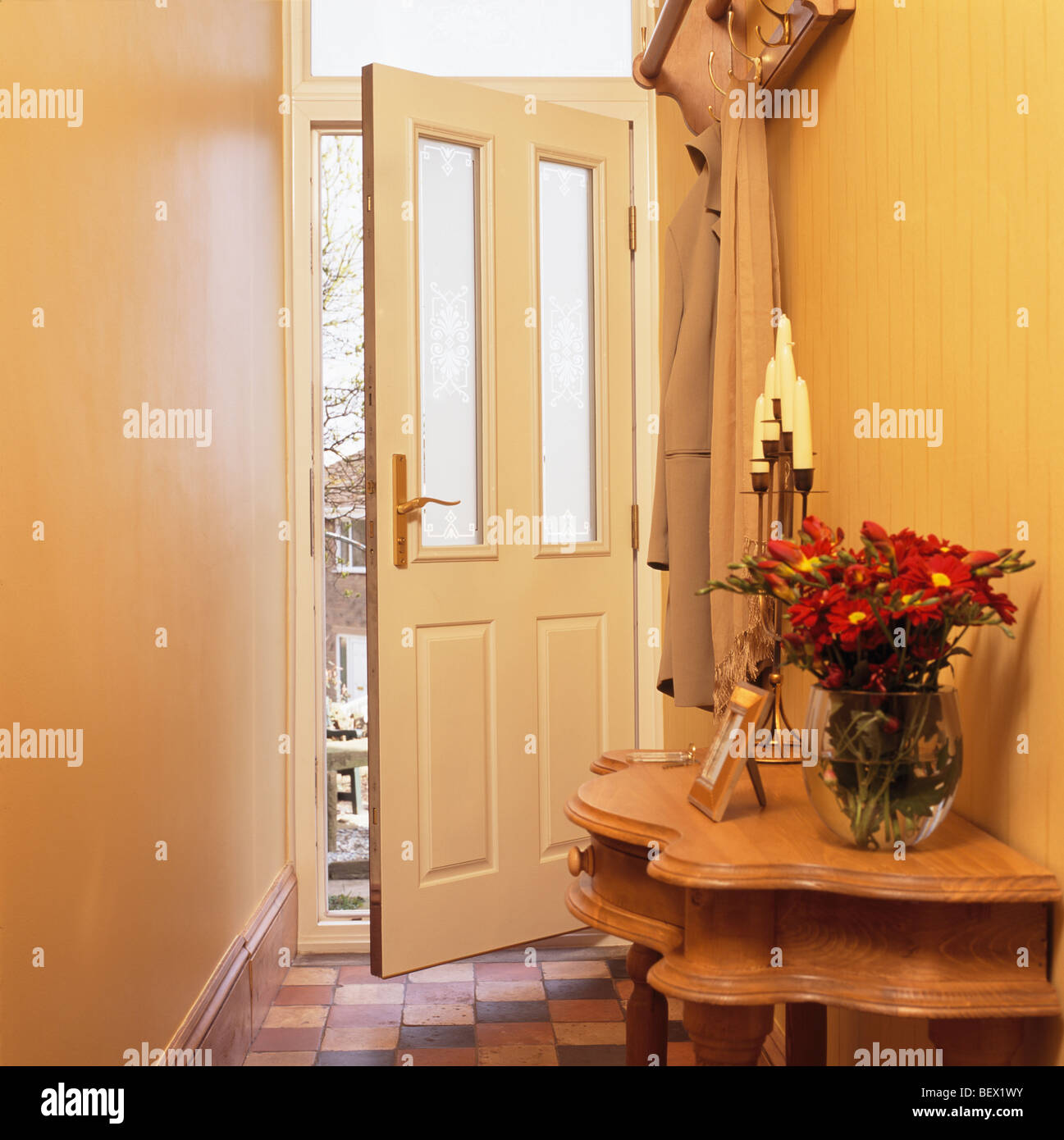 Red flowers in vase on console table in small yellow hall with door