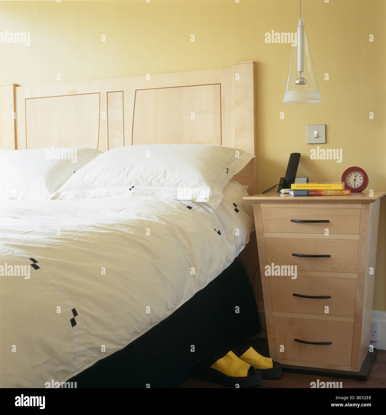 Pale wood beside bed with wooden headboard and patterned white