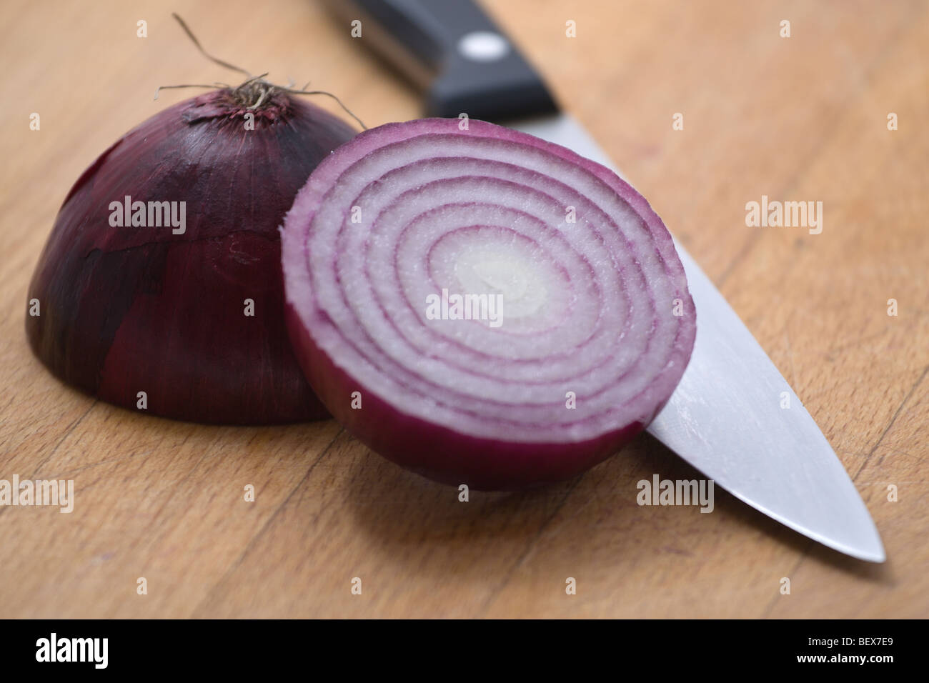 A red onion sliced in half on a chopping board with a knife Stock Photo ...