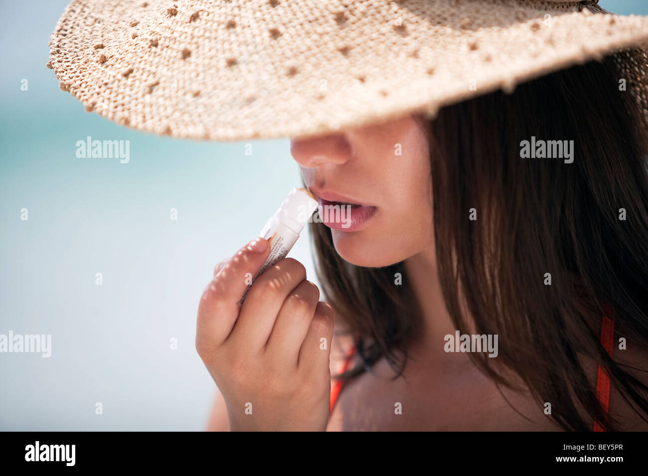 young woman wearing a straw hat, holding lip balm Stock Photo