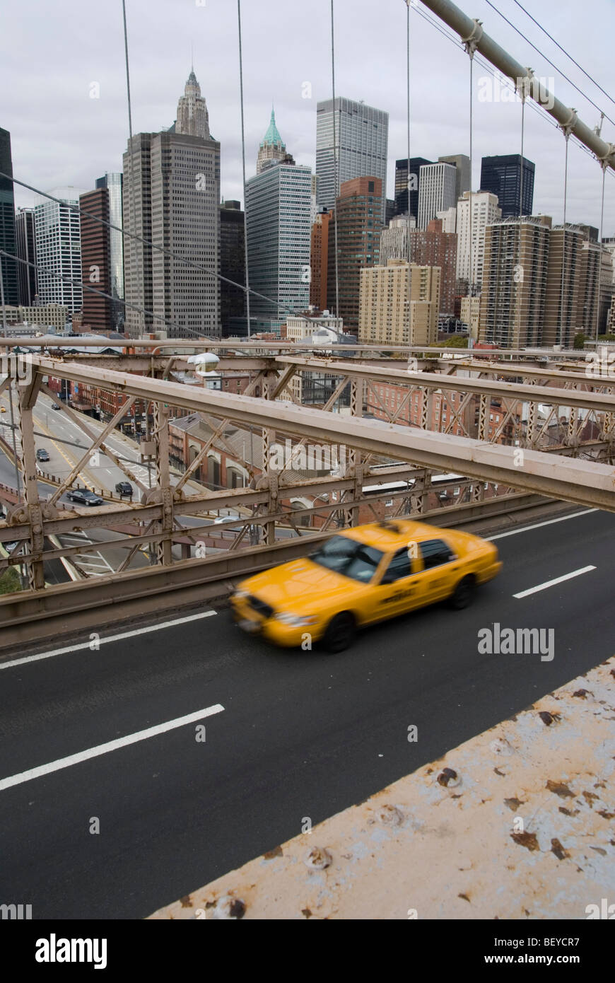 A yellow cab speeding over the Brooklyn Bridge, with the New York City skyline in the background. Stock Photo