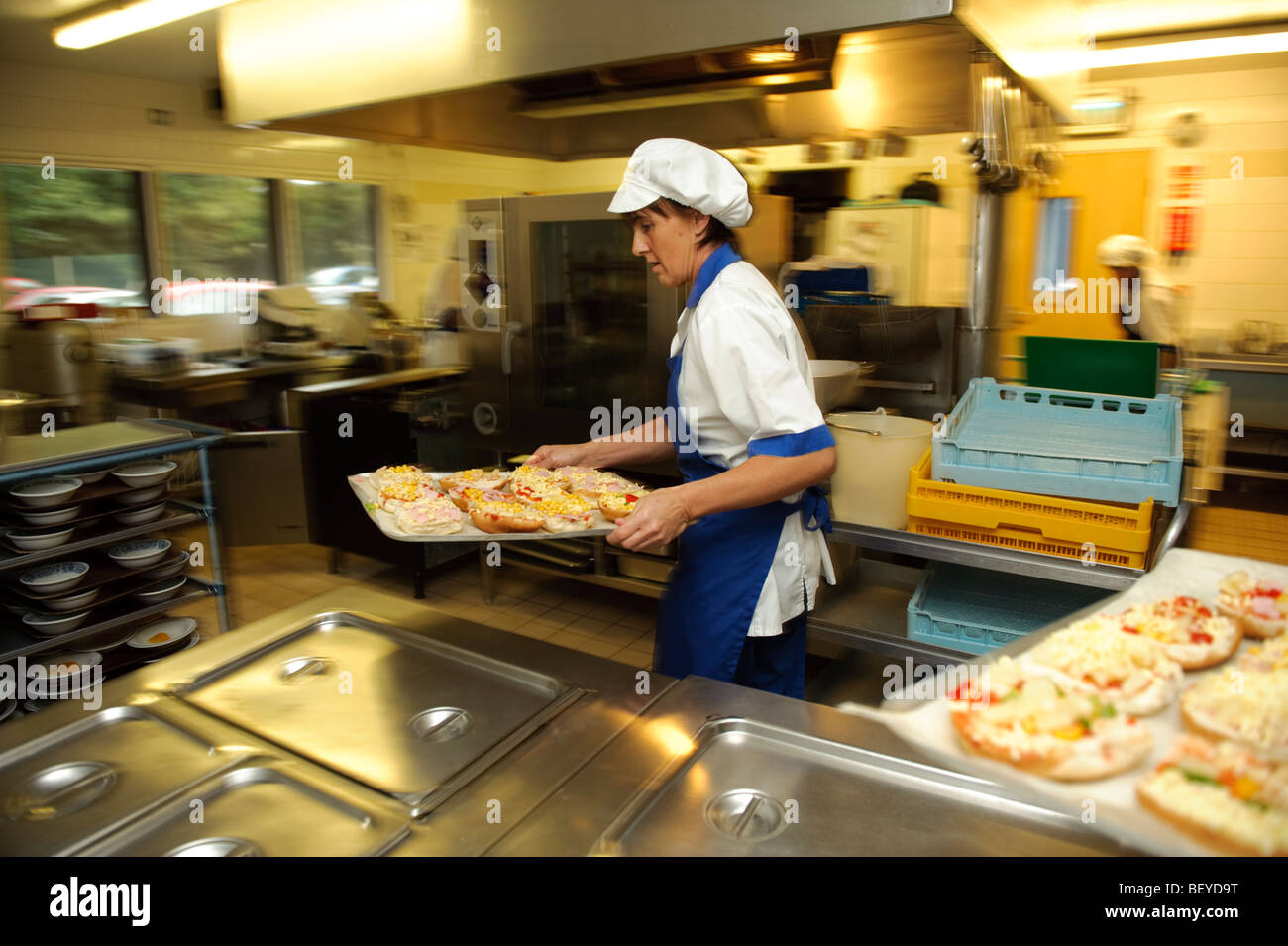 Woman cook in a primary school canteen kitchen about to cook a tray of pizzas for lunch, UK Stock Photo