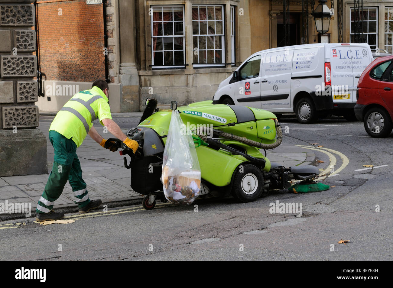 Operative using a walk behind pavement and road sweeper on the sidewalk