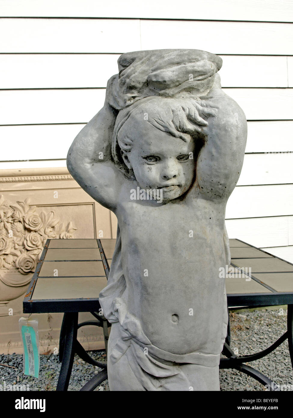 plaster yard garden sculpture of cherub boy with arms in air next to a table for sale Stock Photo