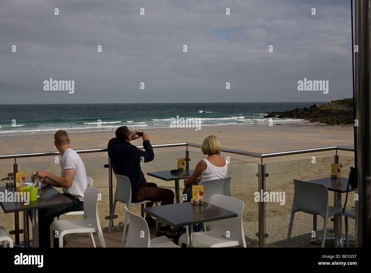people sitting on a balcony of a cafe overlooking Porthmeir Beach, St Ives, Cornwall, England, UK Stock Photo