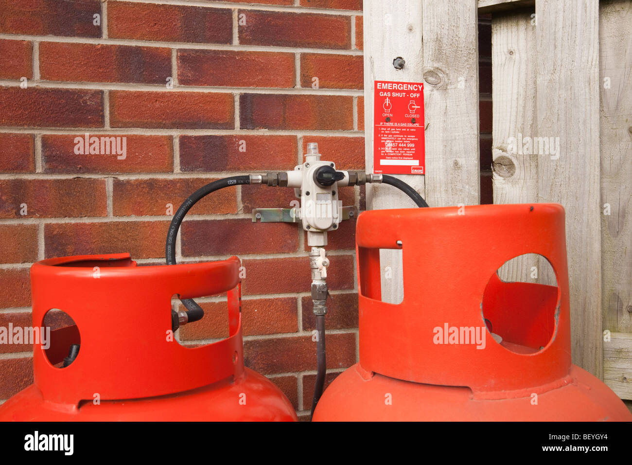 Britain, UK. Calor Gas cylinders and two hose regulator valve fitting on a house wall with emergency gas shut off instructions. Stock Photo