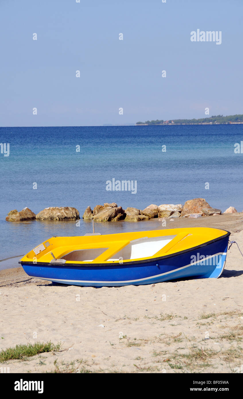 A yellow and blue painted rowing boat on a sandy beach against a blue sky Stock Photo
