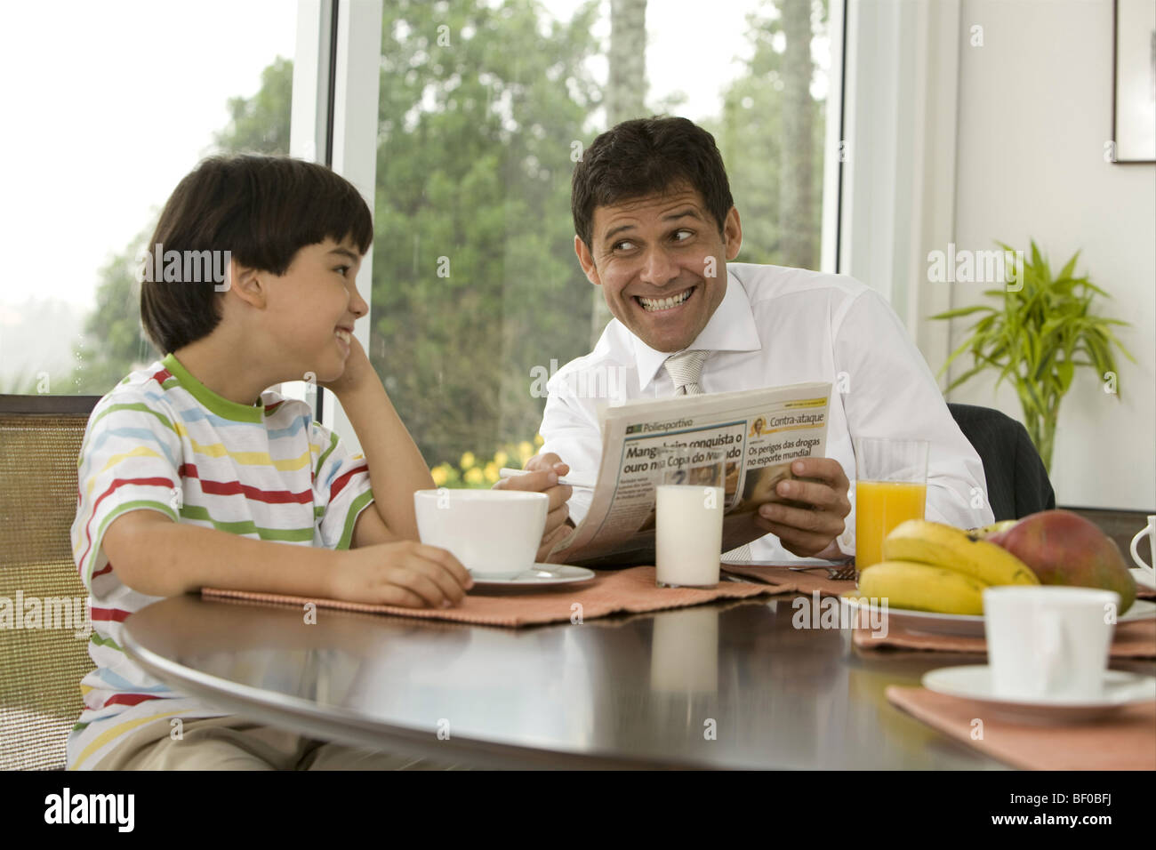 Mature man asking his son for help with puzzle in newspaper at a breakfast table Stock Photo