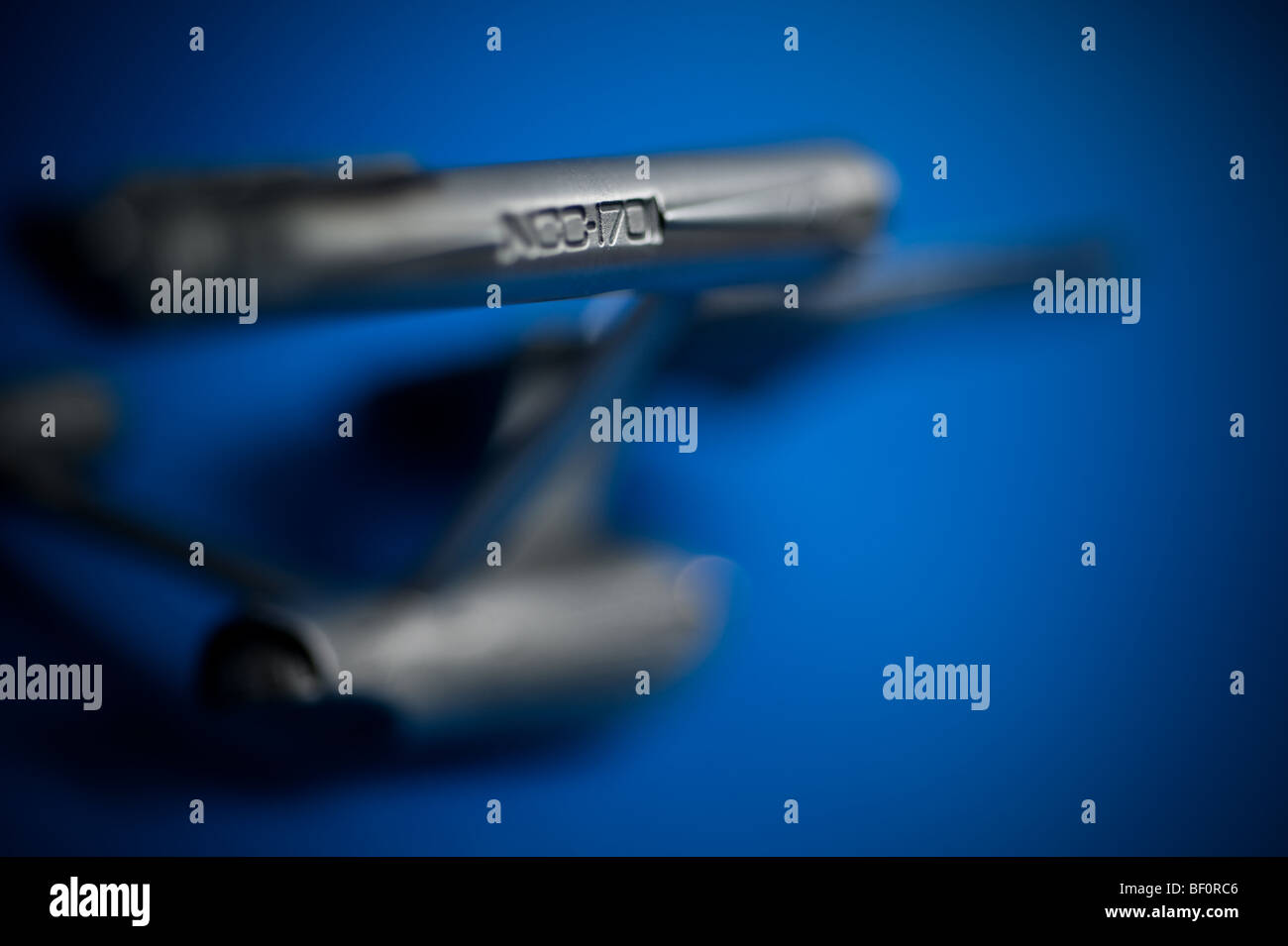 A pewter model of the famous Starship, USS Enterprise, from TV's Star Trek, displayed on a blue background. Stock Photo