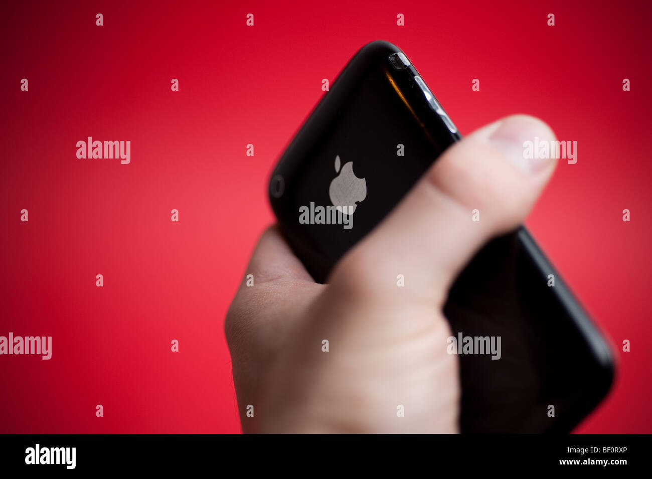 A black Apple iPhone 3G hand held in front of a red background. Stock Photo