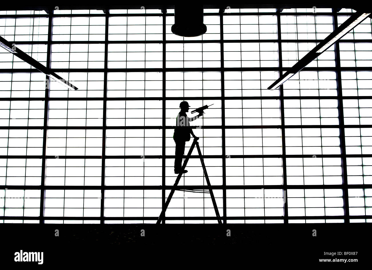 A man on a ladder puts the finishing touches to a large opaque wall in the departures hall in Glasgow Airport, Scotland. Stock Photo