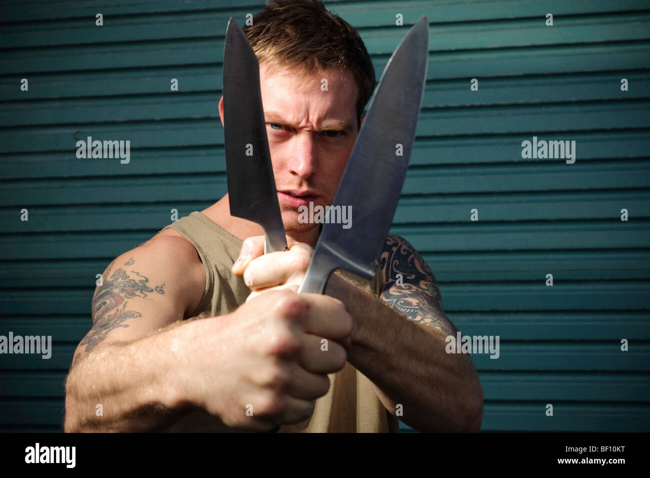 Aggressive 30 year old man with knife - gang member with heavily tattooed arms Stock Photo